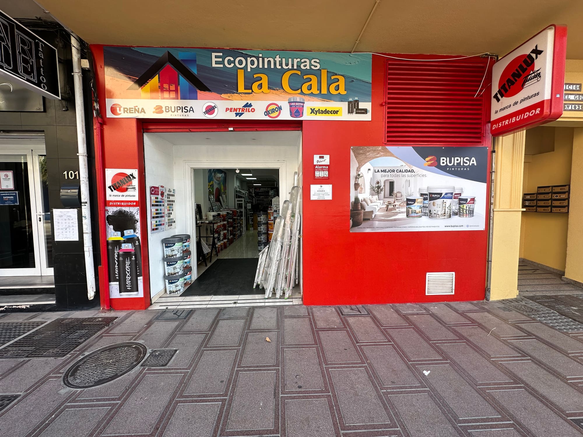Fachada completa de Ecopinturas La Cala en la Avenida de Málaga, 103, con el edificio amarillo encima y el cartel de Titanlux a la derecha.