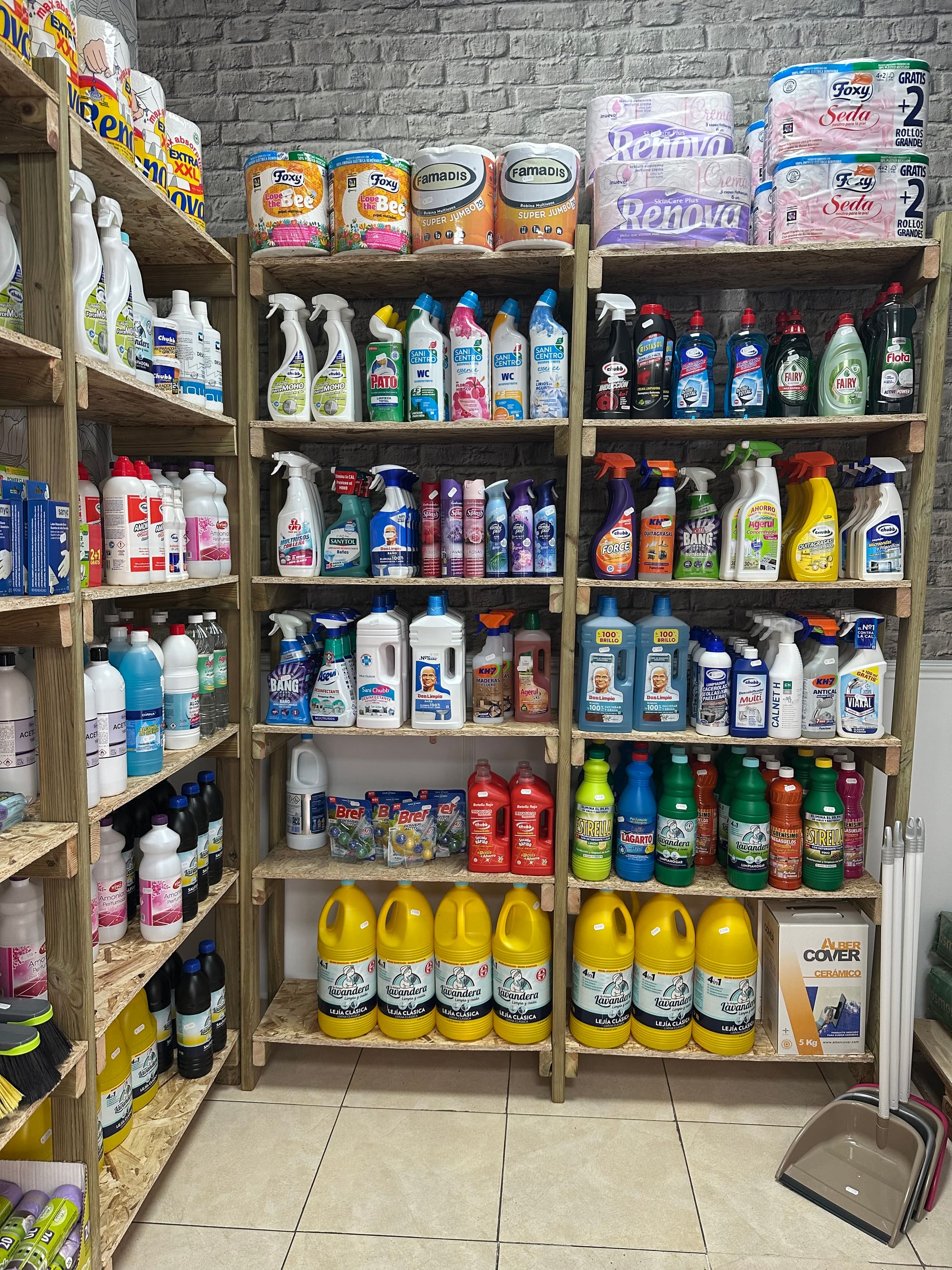 Estantería de droguería con rollos de papel de cocina, limpiadores, lejía y detergentes ordenados por tipo.