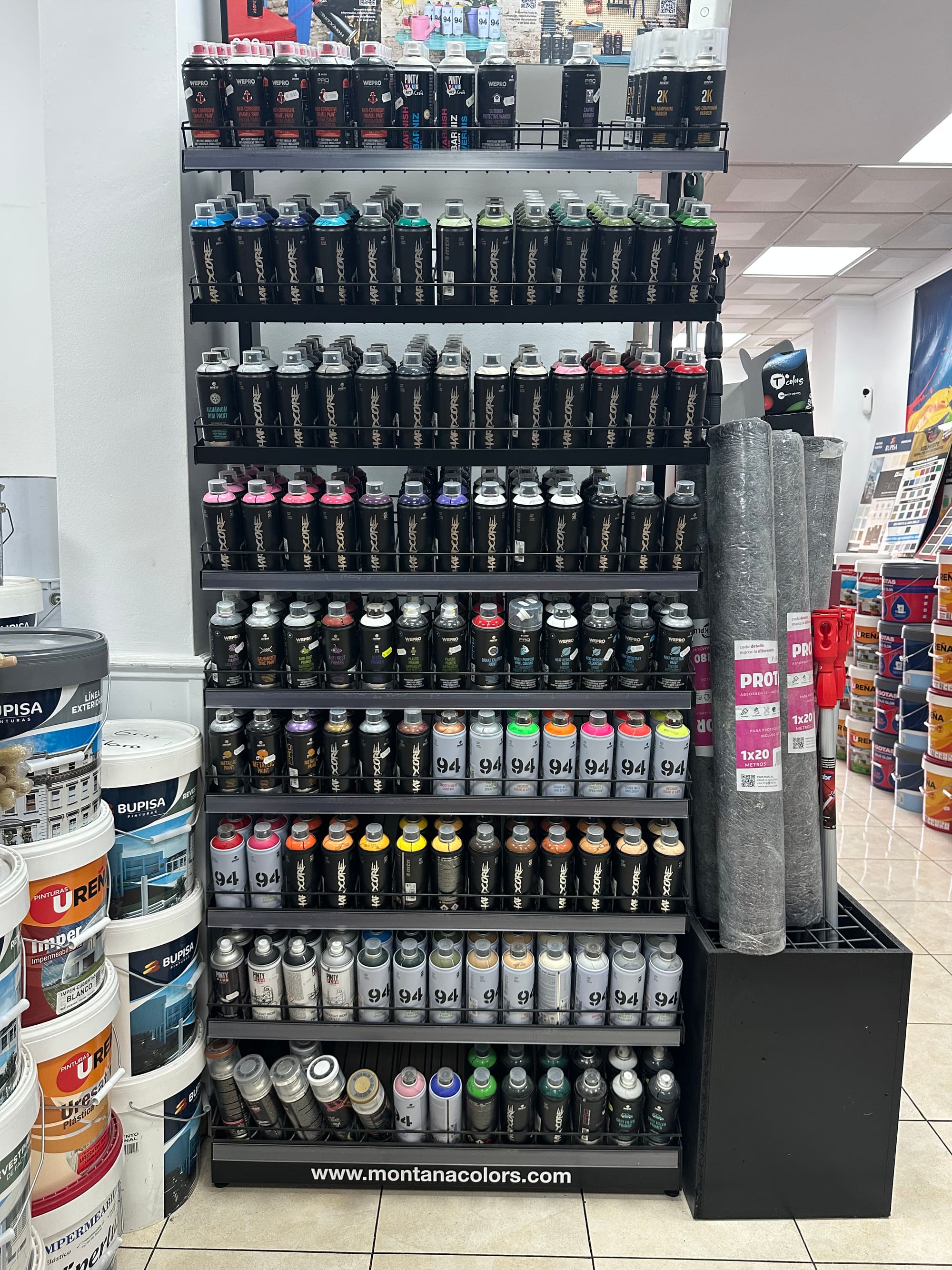 Expositor negro de sprays Montana Colors con cientos de aerosoles ordenados por color, de suelo a techo.