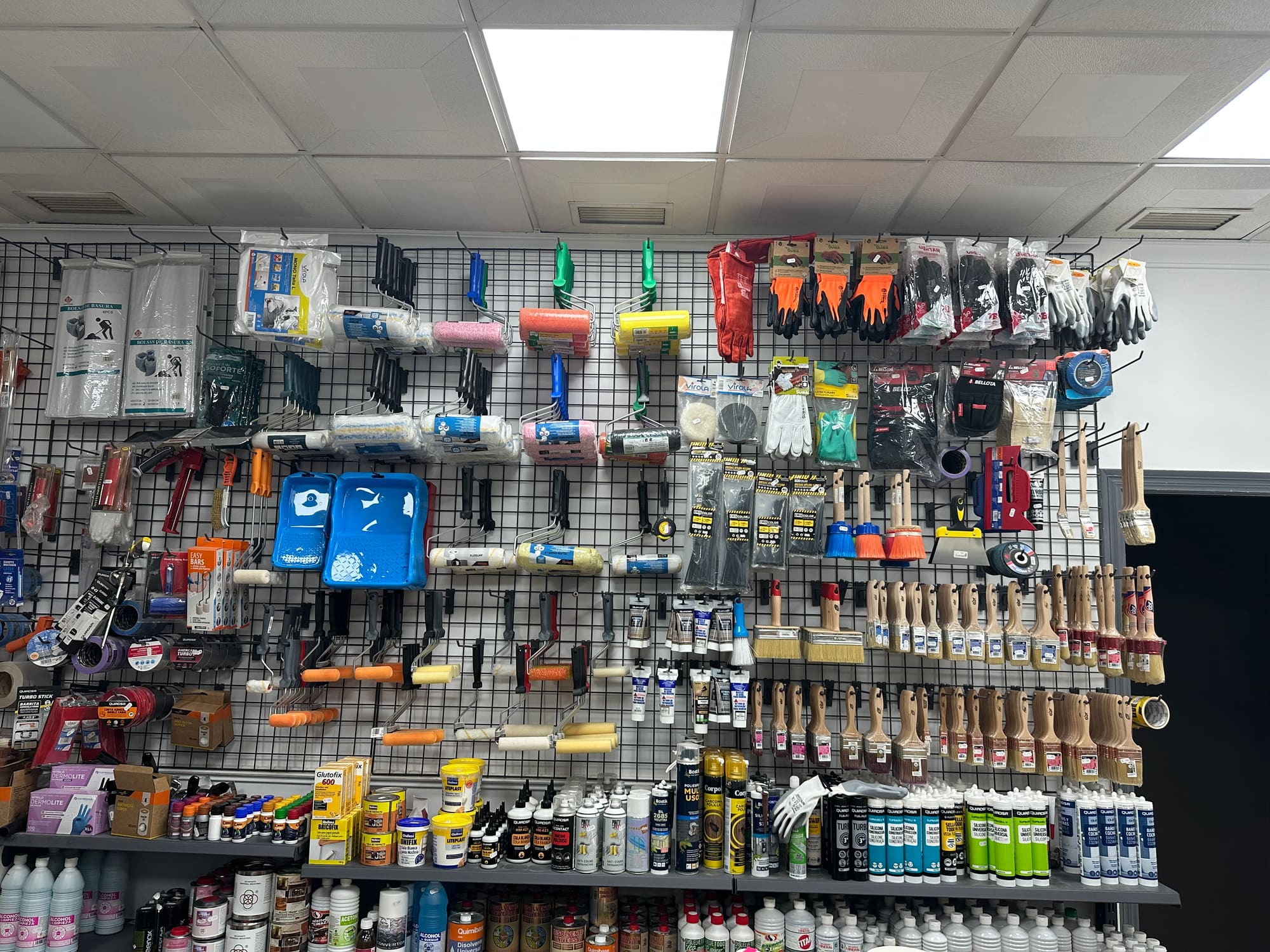 Gran pared de herramientas de Ecopinturas La Cala: rodillos, brochas, cubetas y guantes colgados en el panel perforado.