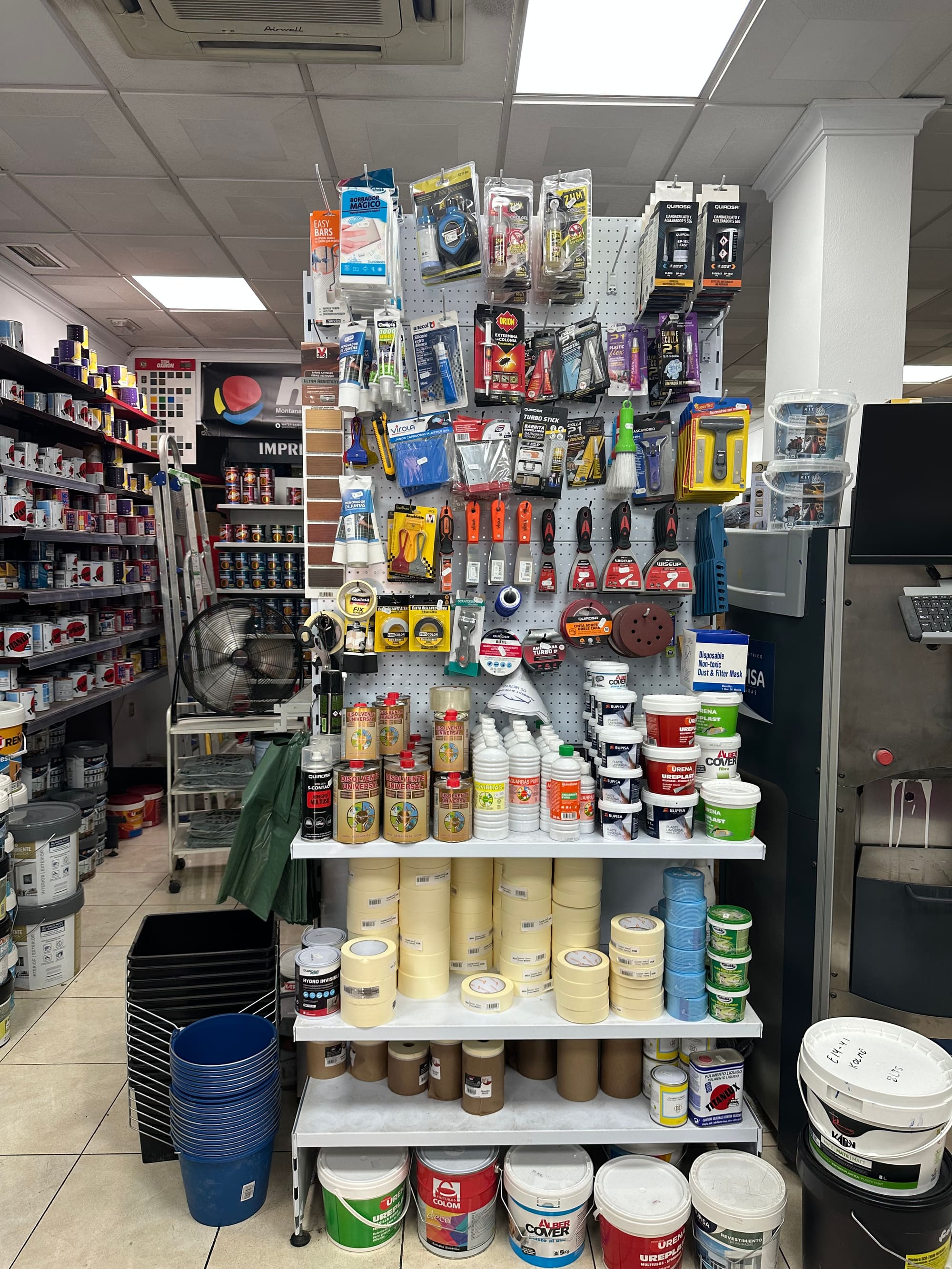 Expositor de accesorios pequeños en blíster y estantería con rollos de cinta de carrocero de varios anchos.